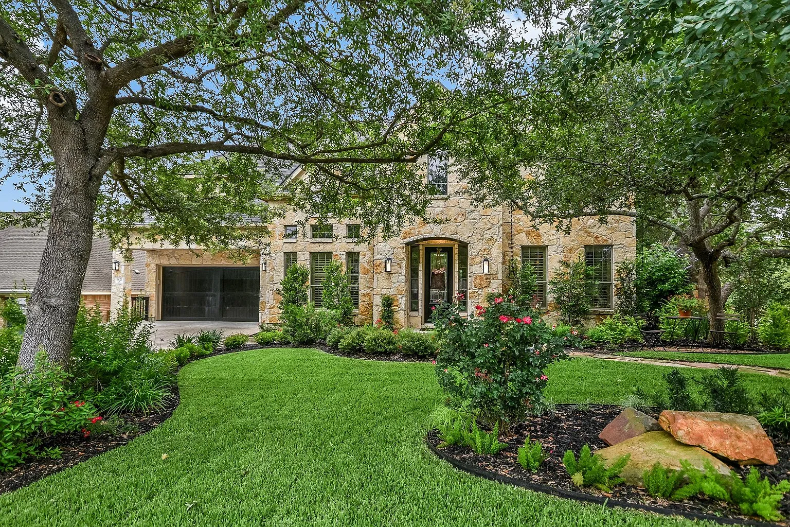 Central Texas stone home with lush manicured lawn, mulched flower beds, and mature oak trees
